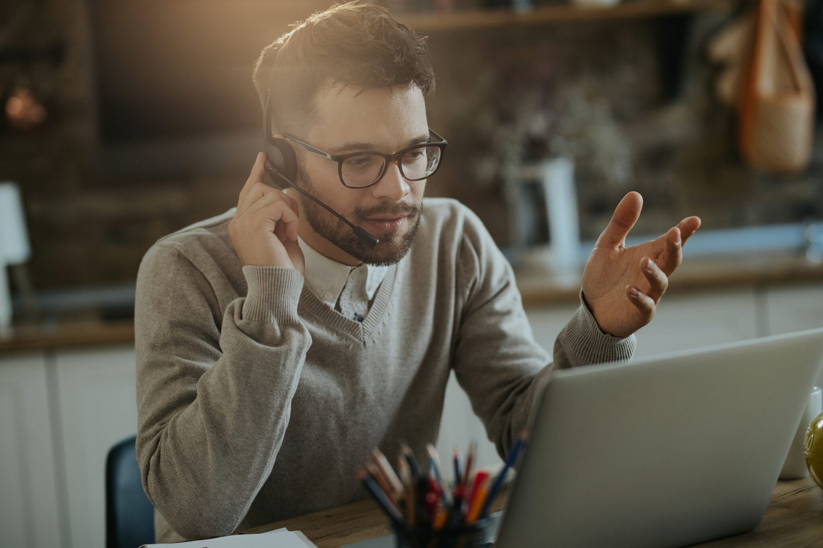 Young businessman with headset talking during video call over laptop at home.