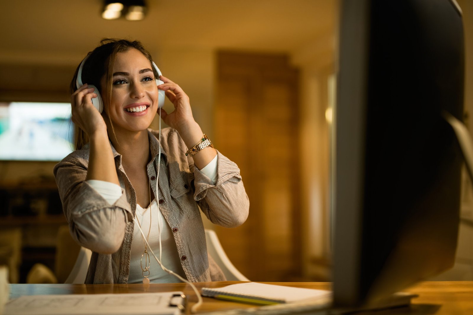 Happy woman relaxing in the evening while wearing headphones and surfing the net on computer at night.